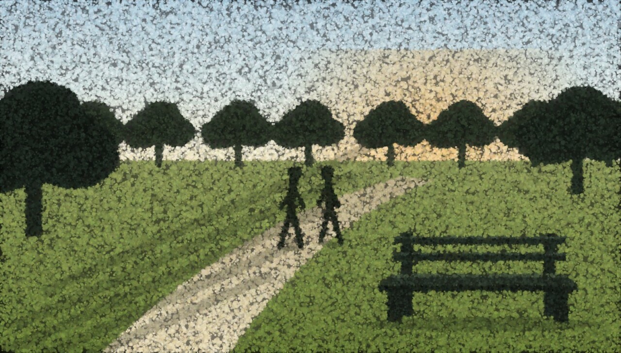 A park path in morning light with two people walking and an empty bench on the grass.
