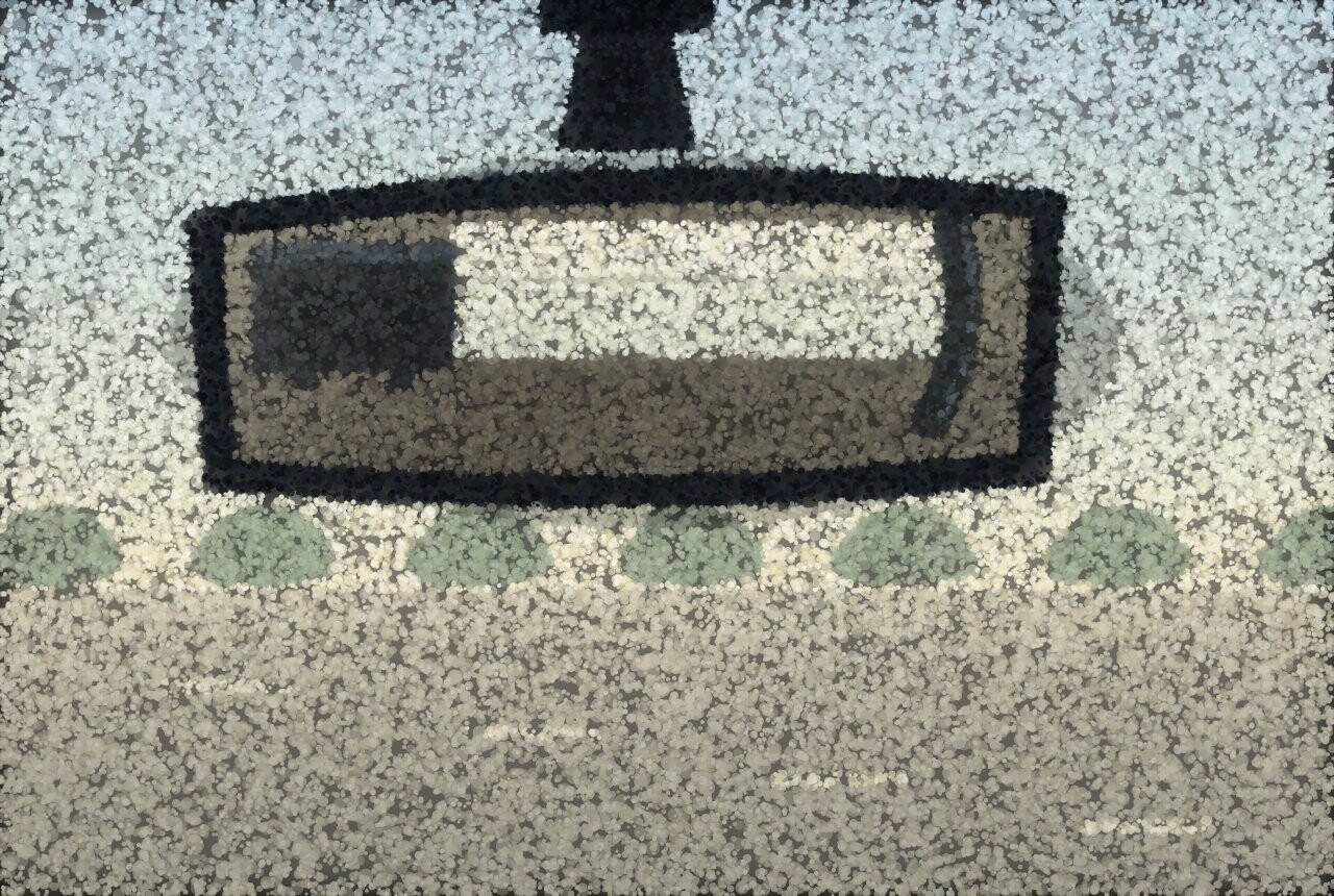 A car rear-view mirror reflecting the back seat and its rear window, with bright road beyond.