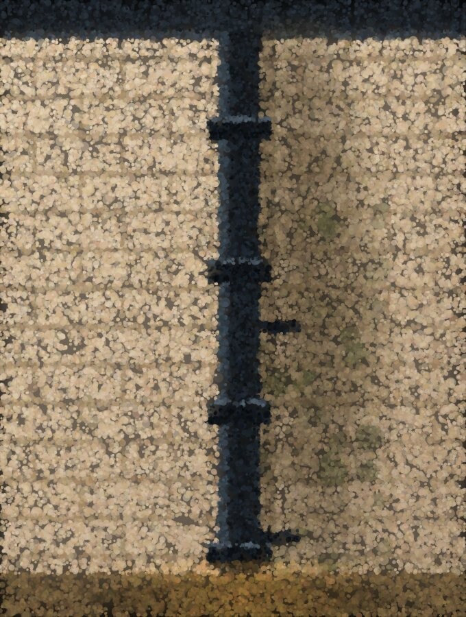 A rainwater downpipe on a brick wall with a dark damp band running down the bricks beside it.