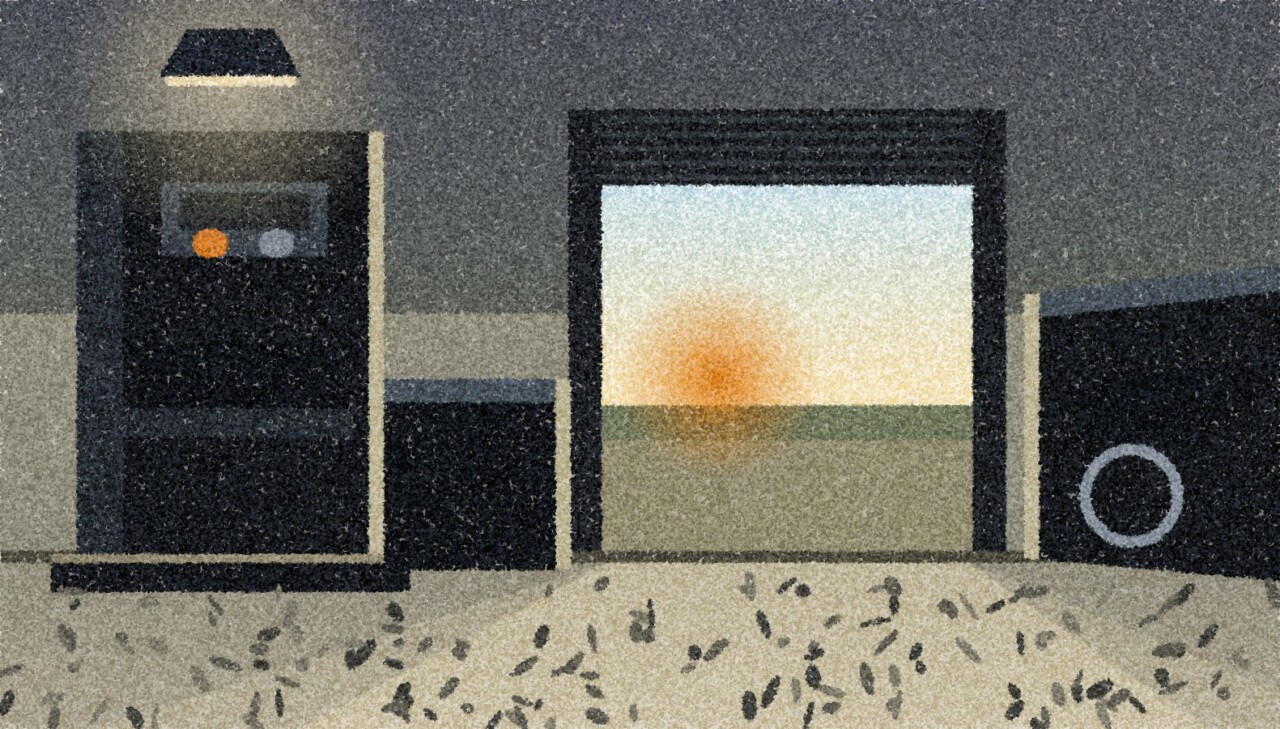 A dark machine shop with a press and other machines standing as silhouettes, the roller shutter door open at the far end and low evening light falling across the floor.