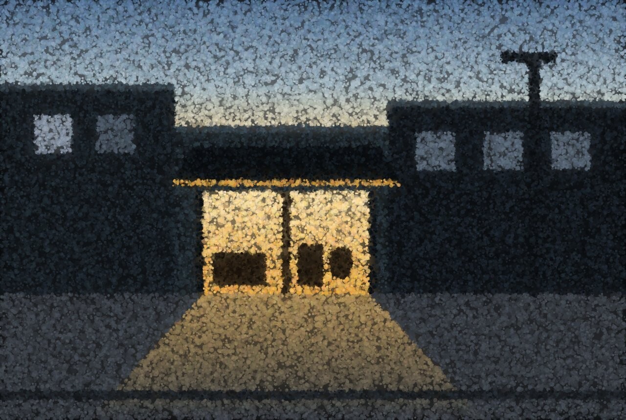 A dark street at dusk with a single warmly lit shop window spilling light onto the pavement.