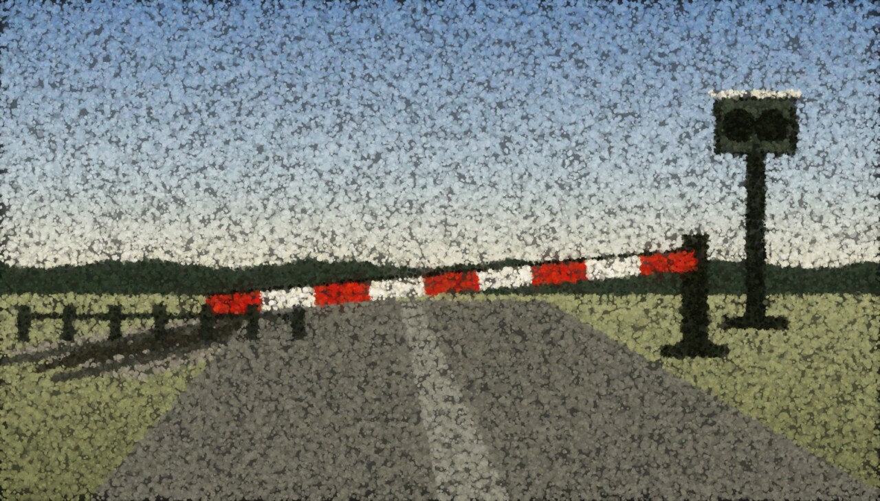 A country level crossing with the striped barrier lowered across the road, rails running off to one side and a signal post against the sky.