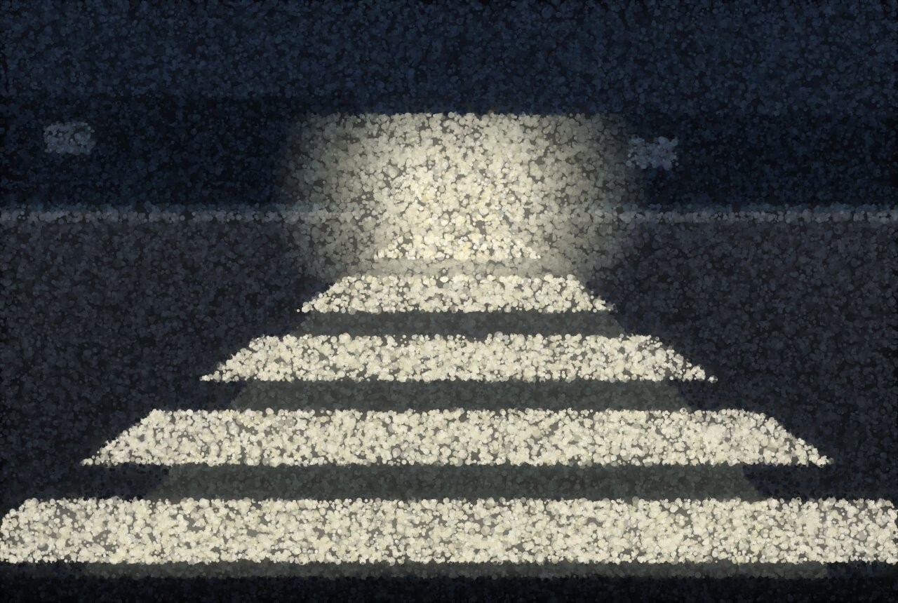 A pedestrian crossing narrowing into the dark, with the glare of oncoming headlights at the far end.