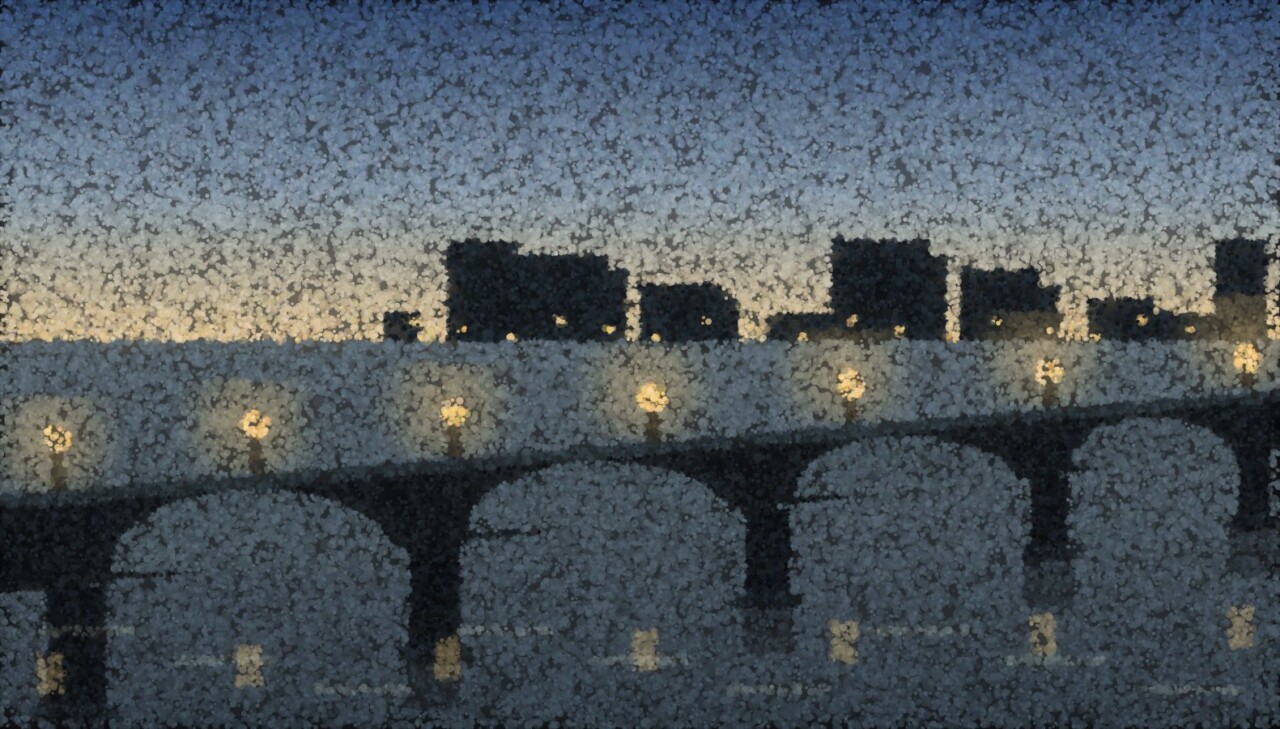 A stone bridge of arches crossing a river at dusk, its lamps lit, the city low on the far bank and everything doubled in the water.