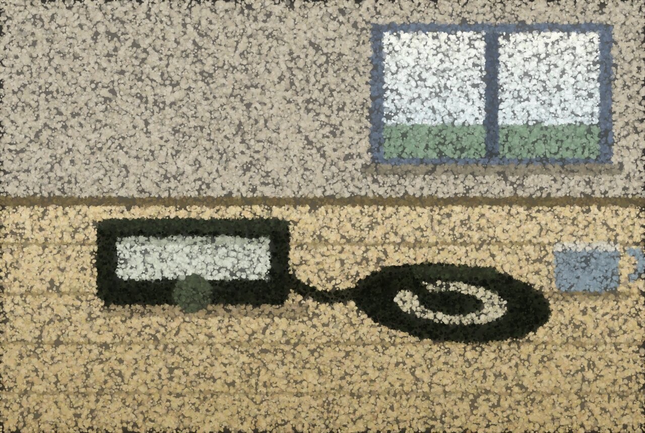 A home blood pressure monitor and its coiled cuff on a wooden kitchen table, with a window behind.