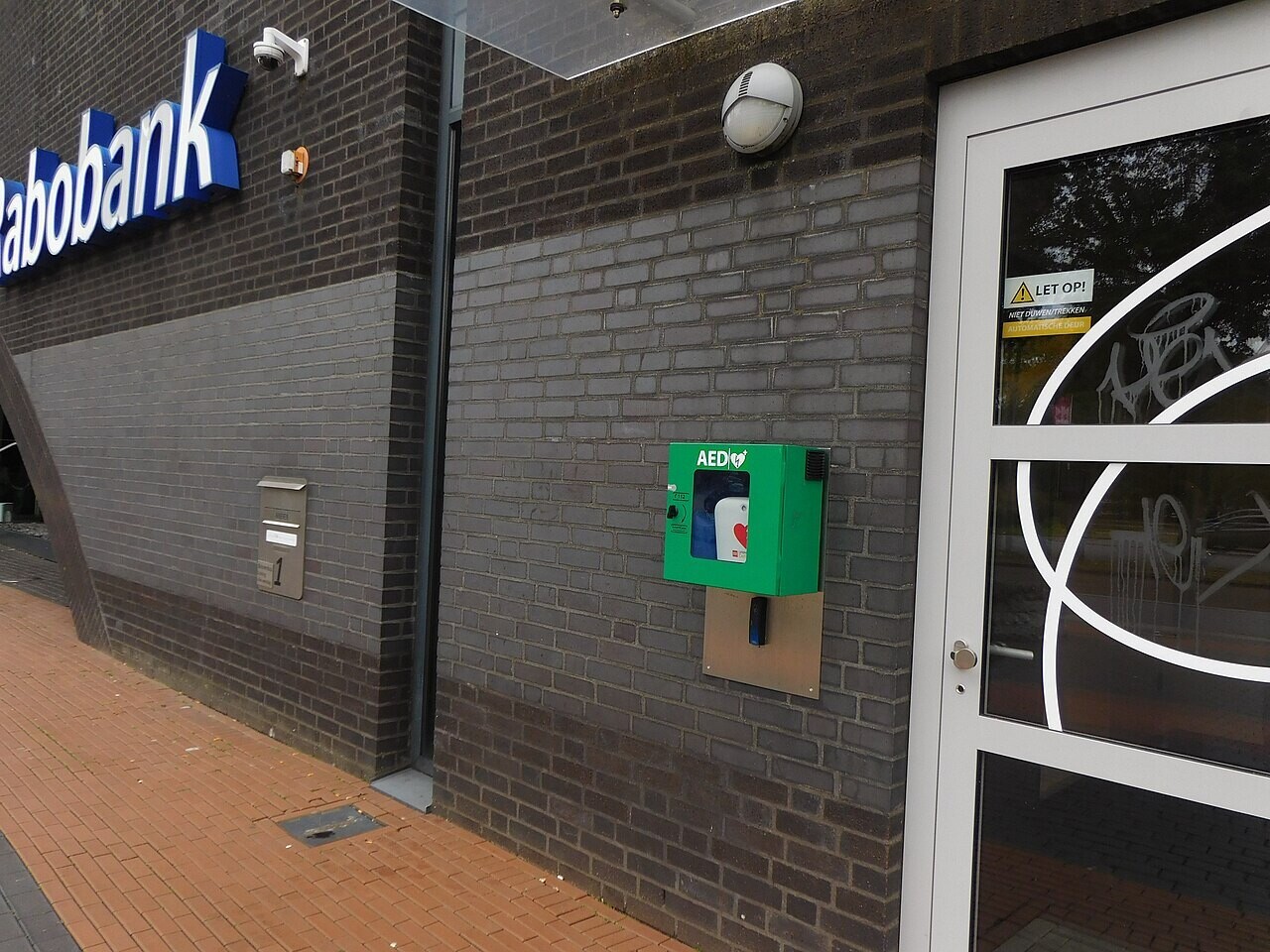 A green public defibrillator cabinet mounted on a brick wall