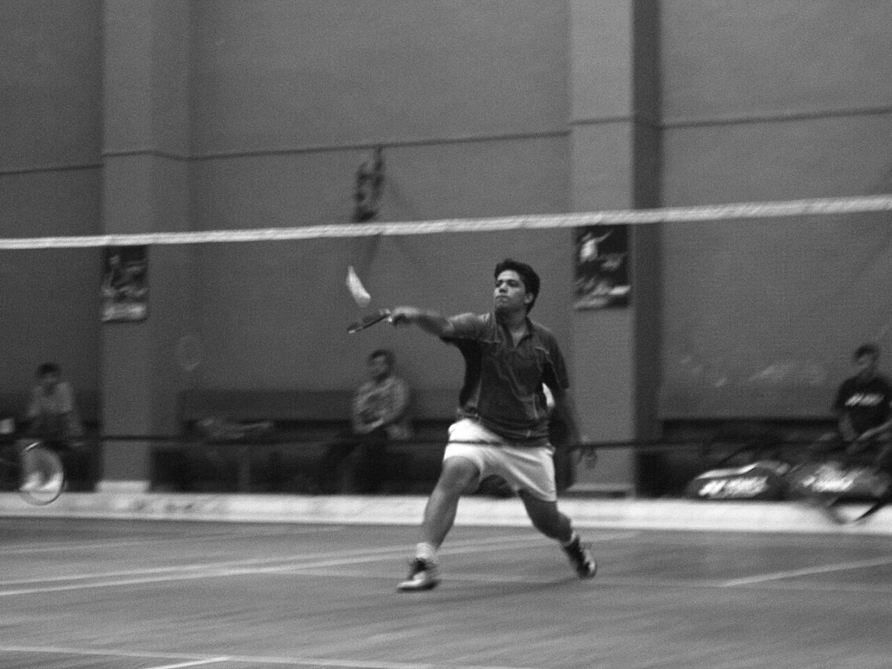 A badminton player stretching to play a shot on an indoor court