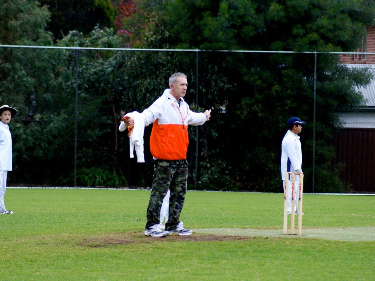 A cricket umpire signalling a wide during a junior match