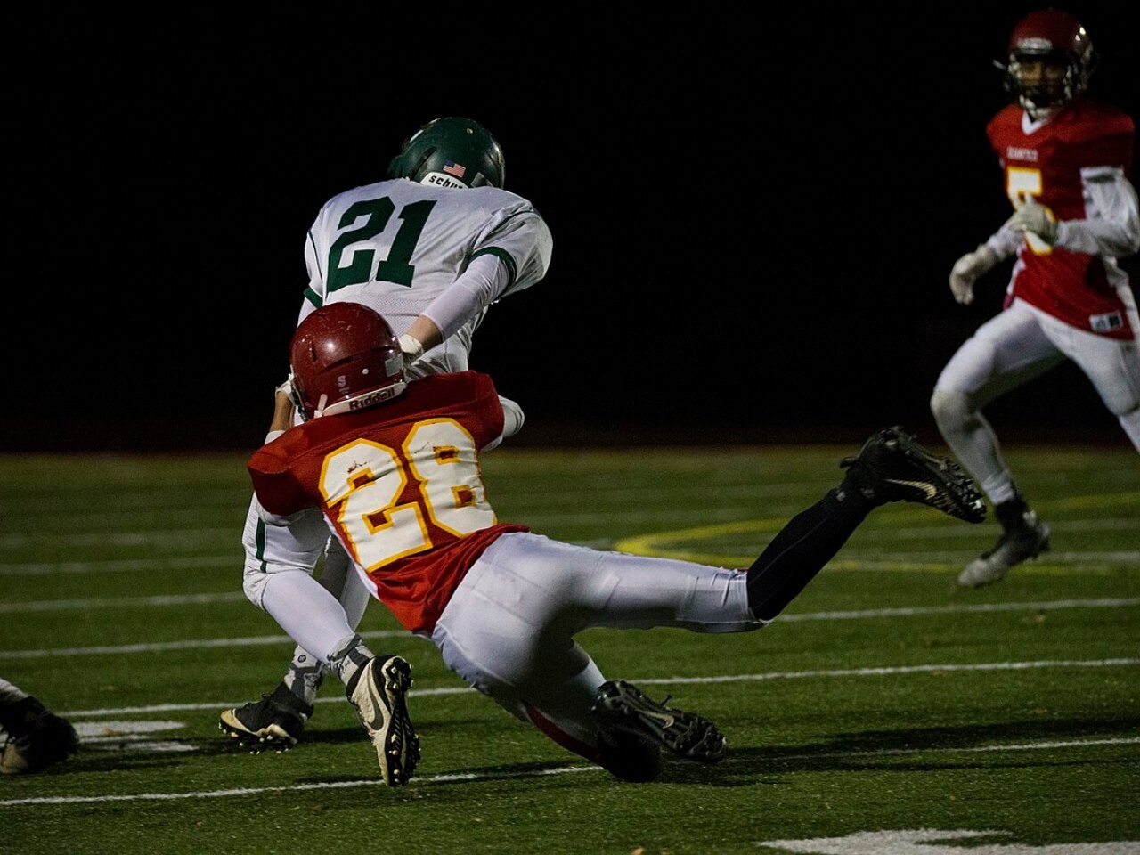 A high school football player making a tackle during a night game