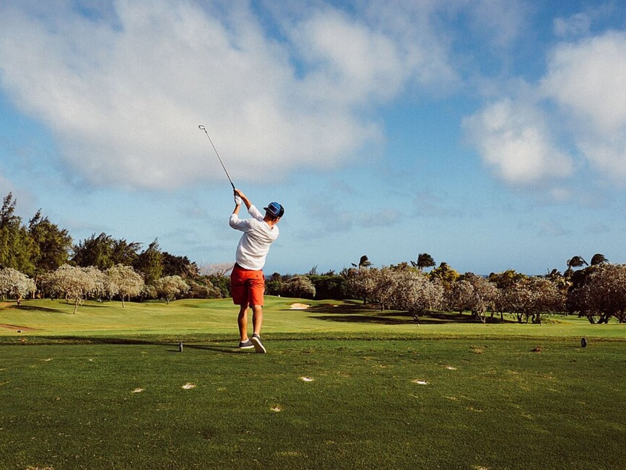 A golfer in a red shirt mid-swing with a driver on a sunny course