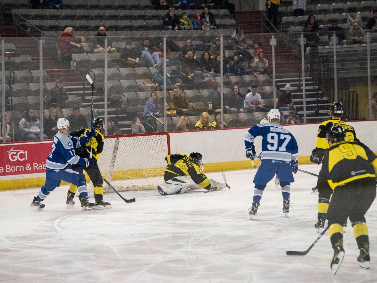 Ice hockey players skating near the net as the goaltender drops to the ice during a game
