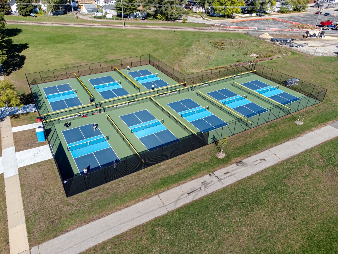 Aerial view of a row of public outdoor pickleball courts beside a park path