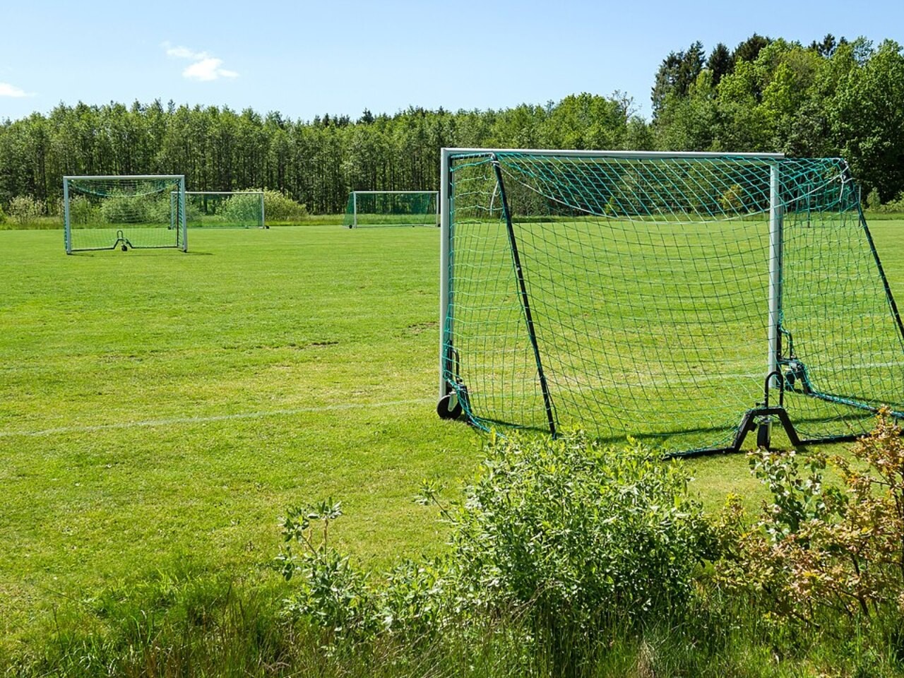 A small movable soccer goal standing on a grass training field