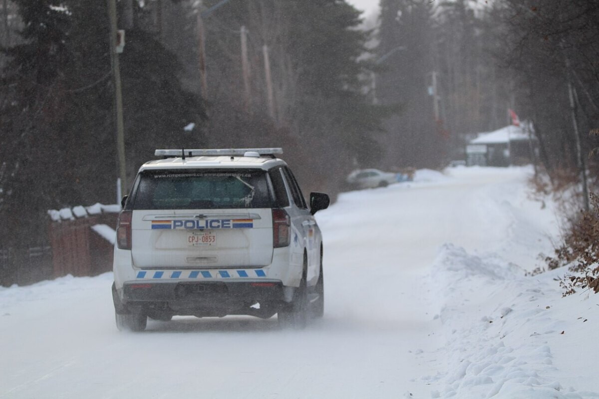 A white RCMP police car driving on a rural road