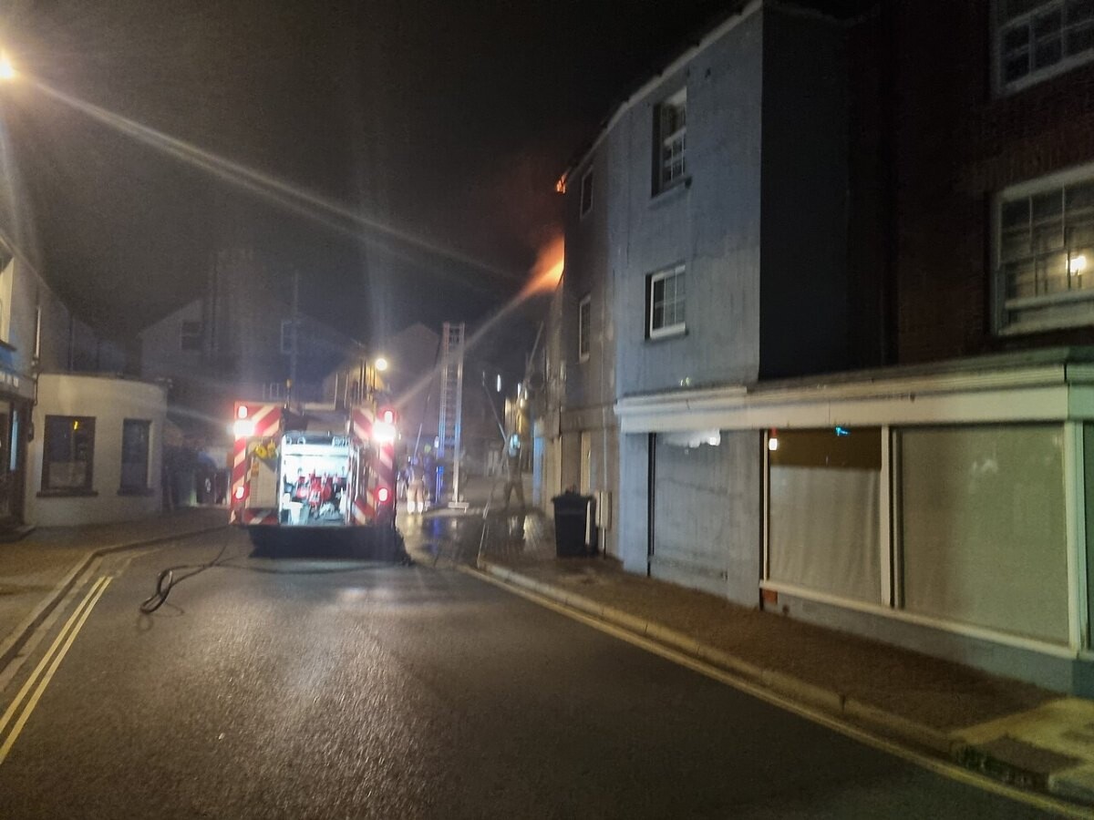 Firefighters and a fire engine at night outside a smoke-filled terrace building