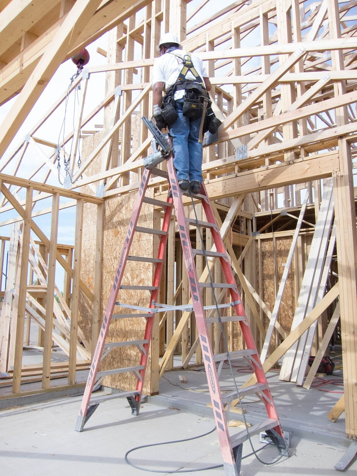 A worker standing on a tall ladder inside a timber house frame