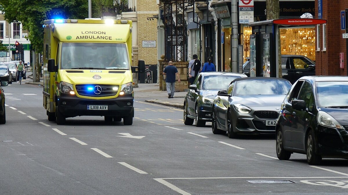 A yellow NHS ambulance driving along a London street