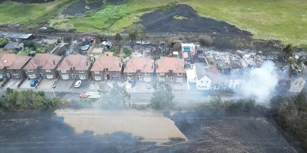 Aerial view of burnt gardens and houses next to scorched grassland