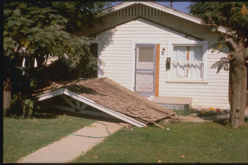 A collapsed wooden porch roof resting on the ground in front of a house
