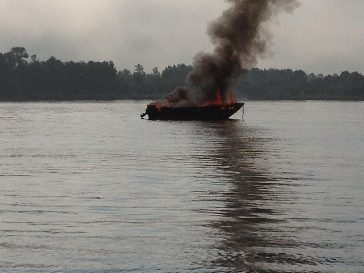 A small pleasure boat burning on a river with dark smoke rising