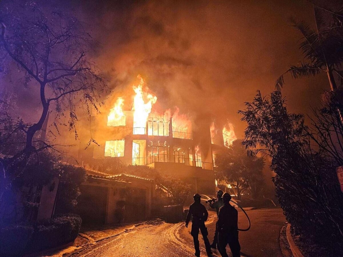 Firefighters silhouetted in front of a burning structure at night